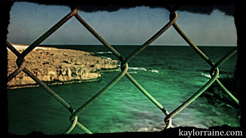chain link fence separating from sea and shore in the distance